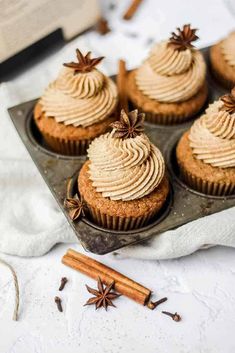 cupcakes with cinnamon butter frosting in a muffin tin next to cinnamon sticks