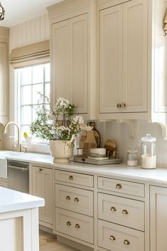 a kitchen filled with lots of white cupboards and counter top space next to a window