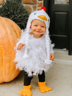 a baby in a chicken costume standing next to a pumpkin