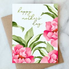 a mother's day card with pink flowers and green leaves on the front, sitting on a marble surface