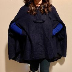 a woman standing in front of a white wall wearing a black and blue ponchy