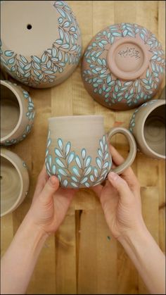 a person holding a coffee cup in front of several pottery pieces on a wooden table