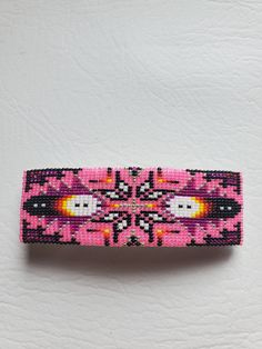 a pink and black beaded hair clip sitting on top of a white surface next to a pair of scissors