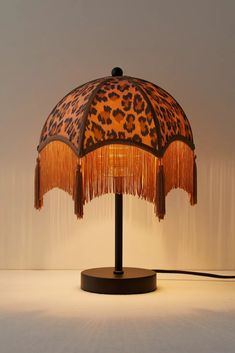 a leopard print lamp with tassels on the base and a light shade over it