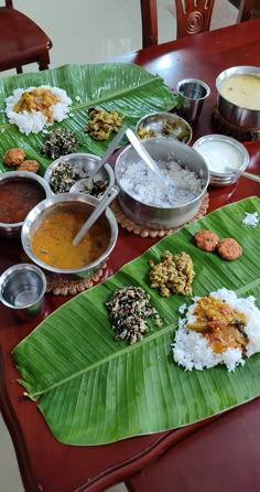 a wooden table topped with lots of food on top of a green leaf covered plate