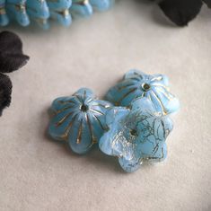 two blue flower shaped beads sitting on top of a white cloth covered table next to black flowers