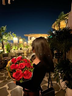 a woman holding a bunch of red roses in her hand and looking at the sky