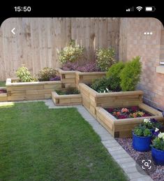 several wooden planters with flowers in them near a brick wall and green grass on the ground