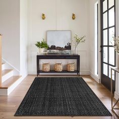 a black rug is on the floor in front of a table with plants and vases