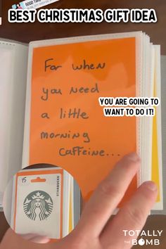 someone is holding up a starbucks gift card in front of an orange book with writing on it