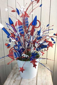 a white bucket filled with red, white and blue flowers on top of a wooden table