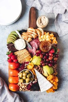 an assortment of cheeses, crackers and fruits on a platter with other food