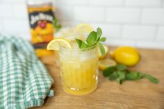 a glass filled with lemonade sitting on top of a wooden table next to sliced lemons