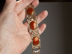 I believe this beautiful bracelet was made in the 1930s. The brass is a rich, gold color and perfectly sets off the caramel-colored oval stones.  The brass panels have a nice weight to them.  The stones could possibly be semi-precious... perhaps brown hematite.   I do see subtle striations.  However, I'll assume they are glass, as I don't have testing equipment.  Also, the photos make them seem a little reddish; they are not.  Caramel brown is more accurate ;-)). This bracelet is in excellent vi Vintage Bronze Bracelet For Formal Occasions, Vintage Bronze Bracelets For Formal Occasions, Gold Oval Bohemian Bracelets, Bohemian Gold Oval Bracelets, Vintage Cabochon Bracelets, Antique Brown Bracelet Gift, Antique Brown Bracelet Ideal For Gifts, Vintage Brown Hallmarked Jewelry, Antique Oval Gold Bracelet