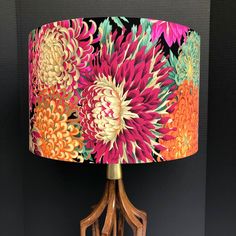 a table lamp with a colorful flower print shade on the bottom and wooden legs, against a black background