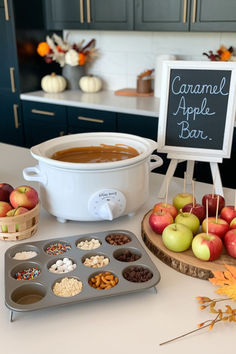 Cozy caramel apple bar setup perfect for a November baby shower, featuring a white slow cooker filled with warm caramel, a selection of apples on a wooden board, and an array of toppings in a muffin tin. The setup is ideal for fall-themed November baby shower ideas and November baby shower food options. Fall Themed Gender Reveal Party Decorations, Fall Themed Party Decorations, Baby Shower Fall Food Ideas, Fall Baby Shower Boy Theme, Baby Shower Girl Theme November, Fall Farmers Market Baby Shower Theme, Baby Shower Ideas Fall Girl, Fall In Love Shower Theme, A Baby Is Brewing Baby Shower Ideas Fall