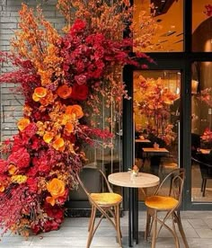 an outdoor cafe with tables and chairs covered in autumn colored flowers on the outside wall