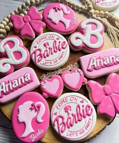 some pink and white decorated cookies are on a wooden plate with beads around it that says, barbie let's go