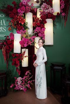 a woman standing in front of a wall with flowers on it and candles hanging from the ceiling