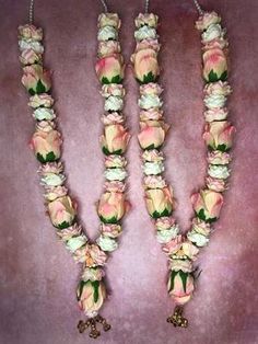 three necklaces with flowers and bells hanging from the side on a pink velvet background