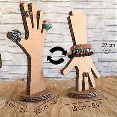 an image of two wooden hand sculptures with beads and rings on each one side, next to a potted plant