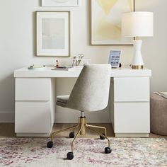 a white desk with a lamp, chair and pictures on the wall in front of it