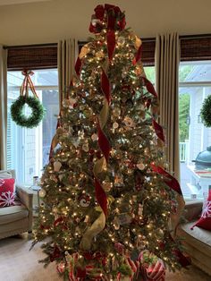 a christmas tree decorated with red and gold ribbons, bows and ornaments in a living room