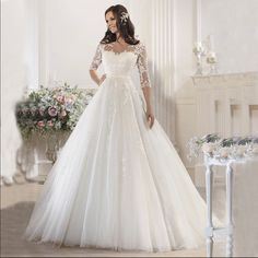 a woman in a white wedding dress standing next to a table with flowers on it