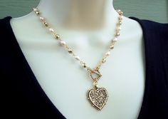 "This lariat style necklace combines a beautiful sculpted heart pendant with freshwater pearls and gold crystal chain.  It features a decorative toggle plated in 24 karat gold which can be worn in the front or the back. This necklace measures 18\" in length. Pendant measures 1 inch. Available in many color stones chain." Gold Beaded Heart Necklace Gift, Gold Beaded Heart Necklace For Gift, Gold Heart-shaped Single Strand Necklace, Gold Single Strand Heart Necklace, Elegant Wire Wrapped Necklaces For Valentine's Day, Gold Wire Wrapped Lariat Necklace As Gift, Elegant Beaded Toggle Necklace As Gift, Elegant Beaded Toggle Necklace For Gifts, Handmade Gold Toggle Necklace With Round Beads