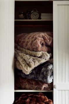 an open closet filled with lots of coats and blankets next to a clock on the wall