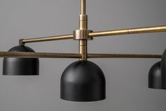 three black and gold colored lights hanging from a metal bar with four shades on each light