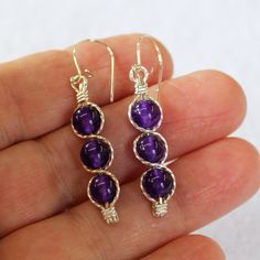 "Three juicy purple 6mm amethyst beads, stacked and outlined with sterling silver wire. This glowing purple shade is one of the hottest colors for the season, and these elegant dangles are sure to get noticed! They measure 1-5/8\" long including the sterling silver kidney earwires. Amethyst is the birthstone for February. Can also be made with 14kt gold filled wire." Wire Wrapped Amethyst Drop Earrings, Silver Amethyst Wire Wrapped Earrings, Purple Wire Wrapped Drop Earrings, Sterling Silver Jewelry With Round Beads And Ear Wire, Adjustable Lavender Sterling Silver Earrings, Hypoallergenic Lavender Sterling Silver Jewelry, Wire Wrapped Amethyst Round Earrings, Amethyst Wire Wrapped Round Earrings, Amethyst Birthstone Dangle Jewelry