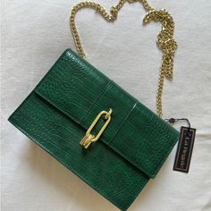 a green purse with a gold chain hanging from it's side on a white surface