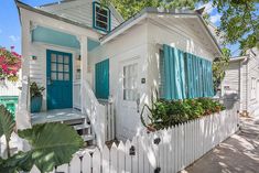 a small white house with blue shutters and flowers in the window boxes on the porch