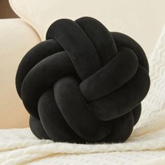 a black knot pillow sitting on top of a white blanket