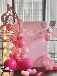 a birthday card with balloons and butterflies on the table in front of a large window