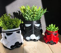 three pots with plants in them sitting on a table next to each other, one is shaped like a storm trooper