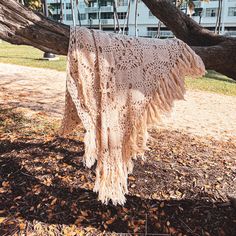 a crocheted shawl hanging on a tree branch in front of a building