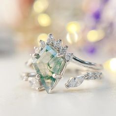 an engagement ring with a green and white stone surrounded by diamond accents on a table