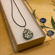 a necklace with blue and white flowers is sitting in a box on the ground next to a tile floor