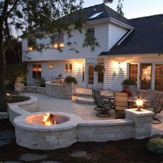 a fire pit in the middle of a patio with chairs around it and lights on