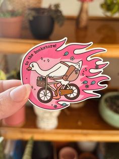 a person holding up a pink sticker with a bird riding a bike on it