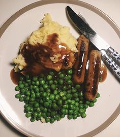 a plate with peas, mashed potatoes and sausage on it next to a knife