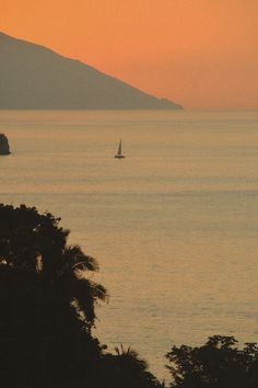 the sun is setting over the ocean with sailboats in the water and hills in the distance