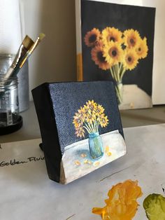 a painting on a table with flowers in a vase and other art work behind it