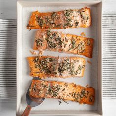 four salmon fillets on a white platter with a serving spoon next to them