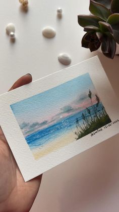 a person holding up a card with an image of the ocean and beach on it