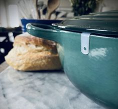 a green casserole dish sitting on top of a counter next to a loaf of bread