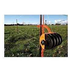 an orange and black pulley is in the middle of a grassy field with a wire fence