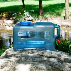 a blue plastic jug sitting on top of a rock next to a river and trees